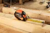 A tape measure is shown on wooden planks, with a screwdriver and a screw in the background. Produktbild-Vorschau