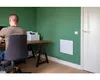A man sits at a desk in a room with green walls, working on a computer. A white heater is mounted on the wall. Náhled obrázku produktu