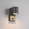 A modern gray outdoor wall light with a motion sensor is mounted on a light gray wall. Produktbild-Vorschau