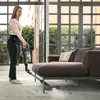 A woman is vacuuming a living room with a cordless vacuum cleaner. Produktbild-Vorschau