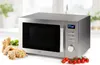 A silver microwave oven is displayed on a white surface with some food items in the foreground. Náhled obrázku produktu