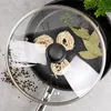 A close-up overhead view of a frying pan with a glass lid, containing uncooked pasta nests, bay leaves, and peppercorns. Produktbild-Vorschau