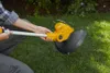 A person is holding a yellow and black string trimmer in a grassy yard. Produktbild-Vorschau