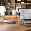 A USB hub and laptop are on a wooden table, with a cup of coffee and a smartphone nearby, in what appears to be a cafe. Anteprima dell’immagine prodotto