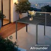 A dark gray square table is set on a tiled patio with a city view in the background. Náhled obrázku produktu