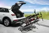 A white car with its trunk open, loaded with bicycles on a bike rack, parked near a beach. Produktbild-Vorschau