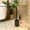 A toilet brush set in a bathroom next to a toilet and a plant. Anteprima dell’immagine prodotto