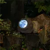 A solar-powered garden light disguised as a rock, nestled among other rocks and foliage. Anteprima dell’immagine prodotto