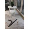 A black infrared heating mat is laid out on a wooden floor next to a rug and a white side table with a potted plant. Náhled obrázku produktu