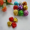 A collection of individually wrapped candies in various metallic foil colors, arranged on a light-colored surface, with some flowers in the background. Produktbild-Vorschau