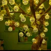 A string of decorative lights shaped like lanterns hangs from tree branches, illuminating a green background. Produktbild-Vorschau