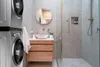 A stacked washing machine and dryer unit next to a bathroom vanity and shower. Podgląd zdjęcia produktu