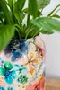 A close-up of a decorative vase with a floral pattern, containing a green plant. Voir les images du produit