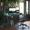 A gaming desk setup in a home office or studio environment, featuring dual monitors, a computer tower, and ambient LED lighting. Produktbild-Vorschau