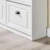 A close-up view of a white wooden shoe cabinet with a black handle on one of its drawers, set against a light-colored wall and wooden floor. Produktbild-Vorschau