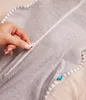 A hand is shown zipping up a gray swaddle for a baby. Produktbild-Vorschau