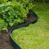 A dark green garden edging strip curves along the edge of a garden bed, separating the soil and plants from a lawn. Produktbild-Vorschau