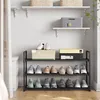 A black metal shoe rack filled with shoes and boxes, placed against a white wall with shelves above. Produktbild-Vorschau