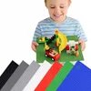 A child is holding a green baseplate with Lego-like toys on it. Several other baseplates of different colors are shown in the foreground. Produktbild-Vorschau