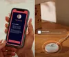 A split image showing a person holding a smartphone with a baby monitor app and a baby monitor device on a wooden surface. Produktbild-Vorschau