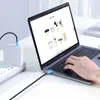 A person is using a laptop that is plugged into a power adapter via a USB-C cable. Produktbild-Vorschau