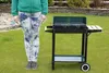 A person stands next to a charcoal grill in a grassy backyard. Produktbild-Vorschau