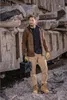 A man stands in a rocky, industrial-like environment, holding a black case. Produktbild-Vorschau
