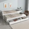 A white daybed with two pull-out drawers is shown in a room with light blue walls and a brown armchair in the background.