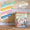 A vintage-style tin can with a retro illustration of a couple, placed on a wooden shelf against a brick wall. Text overlays describe product features. Voir les images du produit
