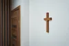 A wooden cross is mounted on a white wall next to a wooden door. Podgląd zdjęcia produktu