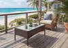 A wicker coffee table and chair on a wooden deck overlooking a beach and ocean. Produktbild-Vorschau