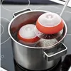 Two orange and white egg poachers are being boiled in a pot of water on a stovetop. Podgląd zdjęcia produktu