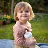 A young child sitting outdoors holding a baby bottle. Anteprima dell’immagine prodotto