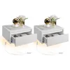 Two white wall-mounted nightstands with open drawers, each featuring a decorative lamp and a vase of flowers on top. Produktbild-Vorschau