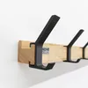 A close-up view of a wooden coat rack with black hooks mounted on a white wall. Voir les images du produit