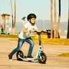 A young person riding a blue Razor kick scooter on a paved path near palm trees and a beach. Anteprima dell’immagine prodotto