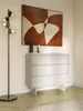 A modern living room scene featuring a greige dresser with three drawers, a floor lamp with glass globes, and abstract art on the wall. Voir les images du produit