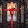 A decorated front door with a large red bow and ribbon, with snow falling. Náhled obrázku produktu