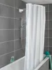 A white shower curtain hangs in a modern bathroom with gray tiled walls and a white bathtub. Produktbild-Vorschau