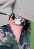A close-up shot of a person's arm wearing a watch and camouflage pants. Podgląd zdjęcia produktu