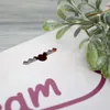 A close-up of a white surface with a decorative cutout and a sprig of artificial greenery. Produktbild-Vorschau