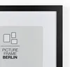 A close-up view of a black picture frame with a white matting and a gray insert showing a graphic and text. Produktbild-Vorschau