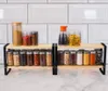 A two-tiered spice rack with various spices in glass jars, set against a white tiled backsplash. Anteprima dell’immagine prodotto