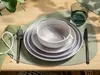 A table setting with plates, a bowl, cutlery, a napkin, and a glass of water on a placemat. Produktbild-Vorschau