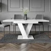 A modern dining table with a white high-gloss finish and a unique V-shaped pedestal base, set in a minimalist dining room with grey walls and chairs. Produktbild-Vorschau