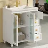A white ceramic sink vanity with gold hardware and fluted glass doors, showcasing storage space. Produktbild-Vorschau