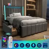 A modern upholstered bed with LED lighting and storage drawers, shown in a bedroom setting with a city view outside the window. A remote control and smartphone app interface for the LED lights are displayed in the foreground. Produktbild-Vorschau