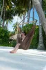 A woman relaxing in a hammock chair under palm trees on a sandy beach. Produktbild-Vorschau