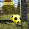 A yellow and black soccer ball rests on green grass in front of a soccer net. Produktbild-Vorschau