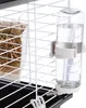 A close-up view of a water bottle attached to the side of a wire cage, with hay in a tray visible on the left. Podgląd zdjęcia produktu